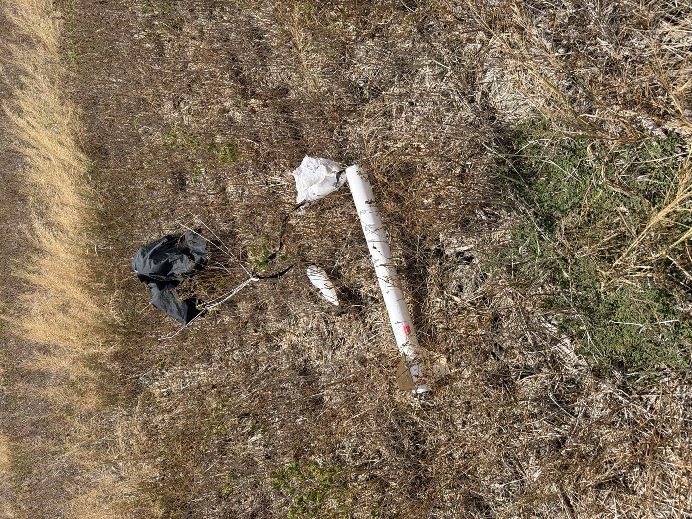 A rocket and its parachute lying in dry grass after landing